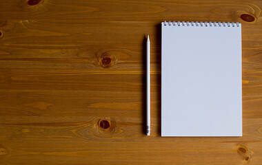 A white notebook and a white pencil on a wooden table.