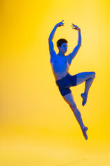 Fototapeta na wymiar Freedom. Young and graceful ballet dancer on yellow studio background in neon light. Art, motion, action, flexibility, inspiration concept. Flexible caucasian ballet dancer, moves in glow.