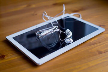 A white tablet and white headphones lie on a wooden table. Remote work from home.