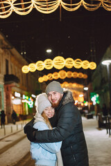 Winter holidays conception. Outdoor night portrait of young couple. Posing in street of European city.