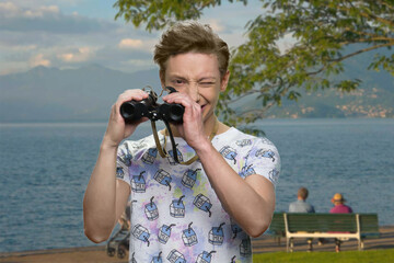 Teen boy with binoculars outdoors. Sea and mountains on the background.