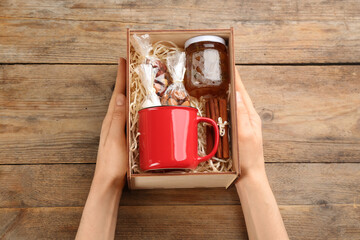 Woman holding box with stylish craft gift set at wooden table, above view