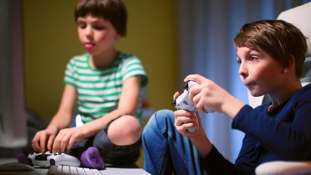 Two brothers are sitting in a room playing video games. Hands using the joystick application control. Getting emotions in your free time at home. Sharp light.