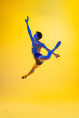 Fototapeta na wymiar Powerful. Young and graceful ballet dancer on yellow studio background in neon light. Art, motion, action, flexibility, inspiration concept. Flexible caucasian ballet dancer, moves in glow.