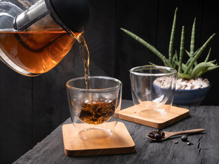 Pouring steam Cascara tea kettle into glass tea cup on dark wood table and background