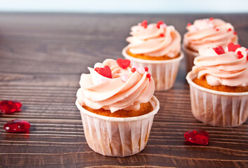 Valentines cupcakes cream cheese frosting decorated with heart shaped candy on the wooden background.
