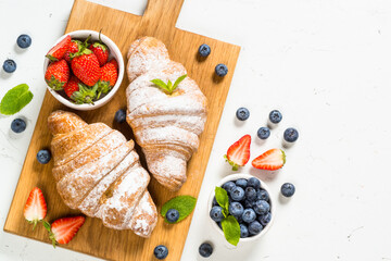 Croissant with fresh berries at white table. Traditional breakfast. Top view.