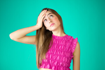 Portrait of preoccupied worried young girl in pink shirt putting hand on head isolated over green background. People lifestyle concept. Mock up copy space