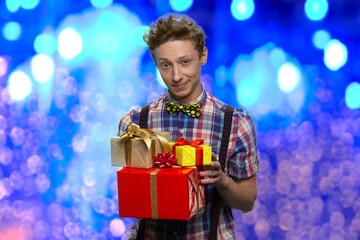 Confident teenager in checkered shirt is holding gift boxes. Bright blue lights on the background.