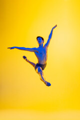 Inspiration. Young and graceful ballet dancer on yellow studio background in neon light. Art, motion, action, flexibility, inspiration concept. Flexible caucasian ballet dancer, moves in glow.