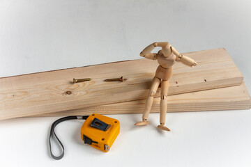 a wooden mannequin sitting on wood boards with self-tapping screws and a tape measure and worrying about repair