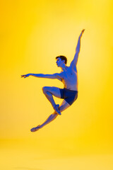 Fototapeta na wymiar Inspiration. Young and graceful ballet dancer on yellow studio background in neon light. Art, motion, action, flexibility, inspiration concept. Flexible caucasian ballet dancer, moves in glow.