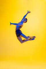 Artwork. Young and graceful ballet dancer on yellow studio background in neon light. Art, motion, action, flexibility, inspiration concept. Flexible caucasian ballet dancer, moves in glow.