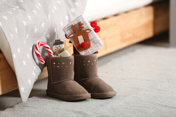 Sweets and gift box in child's boots near bed indoors. St. Nicholas Day tradition