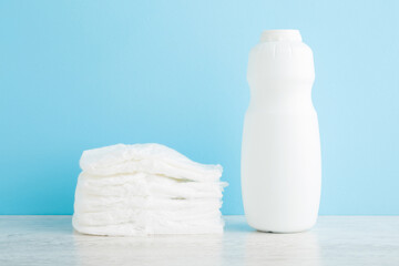White bottle of talcum powder and stack of diapers on wooden table at light blue wall background. Pastel color. Baby skin protection before diaper changing. Closeup. Front view.
