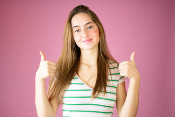 Smiling pretty young girl showing thumbs up isolated over pink background