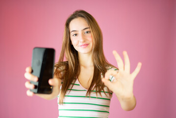 Portrait of a smiling casual girl holding smartphone over pink background
