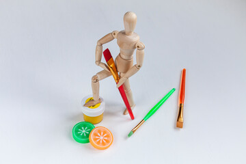 a wooden mannequin with bright colorful brushes, erasers, and a jar of yellow gouache