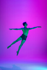 Fototapeta na wymiar Flying. Young and graceful ballet dancer on purple studio background in neon light. Art, motion, action, flexibility, inspiration concept. Flexible caucasian ballet dancer, moves in glow.