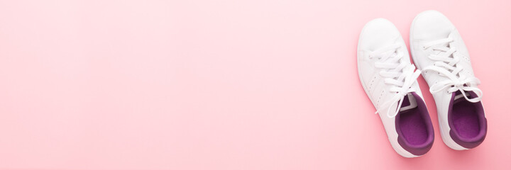 White female sport shoes for walking, running or fitness on light pink table background. Pastel color. Closeup. Wide banner. Empty place for text. Top down view.