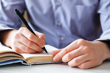 A young business man makes notes with a pen in a notebook as a reminder of important things - Hands and notebook close-up on a table in a home or office - Education and notes with written text
