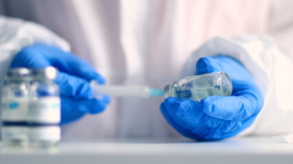 Fototapeta premium Doctor in blue latex gloves fill in syringe with medicine from glass vial for injection of an elderly person in a medical laboratory against coronavirus, flu, measles disease