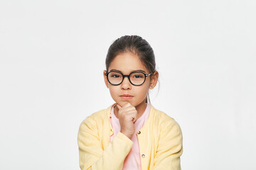 Portrait of a mixed race little girl wearing red glasses with fist under chin, she earnest looks at camera