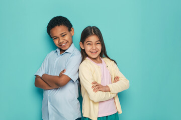 African American boy and Latino girl standing back to back with arms crossed on a turquoise background