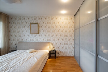 Fototapeta na wymiar COntemporary interior of bedroom in luxury flat. Cozy bed. Nightstands. Huge sliding door wardrobe.