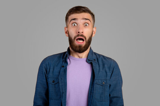 Shocked bearded guy looking at camera in panic over grey studio background