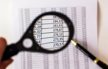 Financial documents with a magnifying glass and a pen lie on a white background.