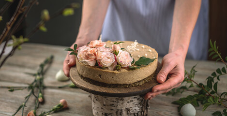 Woman is holding in her hands a beautiful raw mousse cake decorated with tenderness flowers. Concept of a romantic atmosphere and spring mood
