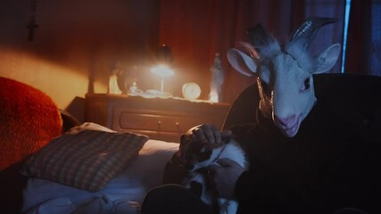 Eerie scene of a scary, masked stranger sitting in a dark living room, petting a cat. Mysterious man in an animal mask, goat costume. Devil waiting in the night, dark, unsettling scene.
