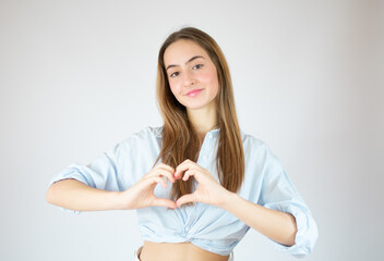 Young girl in blue shirt making heart figure over white background.