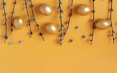 Willow branches with golden eggs lie on top on a yellow background, space for text