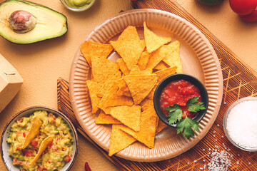 Plate with tasty nachos and sauces on color background