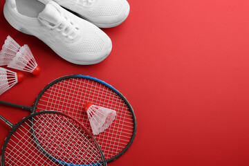 Badminton rackets, shuttlecocks and shoes on red background, flat lay. Space for text
