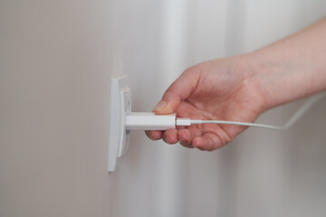 A young girl inserts a plug into an outlet. Young woman plugs the phone charger into the socket. High quality photo