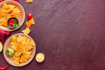 Plates with tasty nachos and sauces on dark background