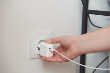 A young girl inserts a plug into an outlet. Young woman plugs the phone charger into the socket. High quality photo