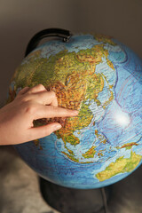 A young woman points her finger at a country on the globe. Globe inscriptions in Russian - names of countries and oceans.