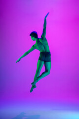 Fototapeta na wymiar Power. Young and graceful ballet dancer on purple studio background in neon light. Art, motion, action, flexibility, inspiration concept. Flexible caucasian ballet dancer, moves in glow.