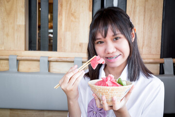 A girl teenage shows a raw tuna uses chopsticks from salmon don in a Japanese restaurant.