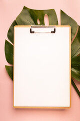 clipboard and monstera leaf on pink background. Flat lay, top view, copy space.