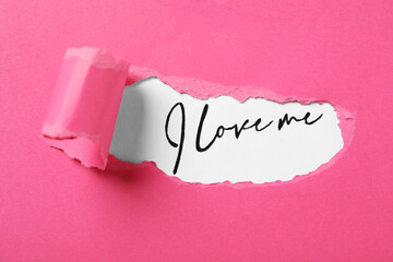 Handwritten phrase I Love Me through torn pink paper on white background, top view