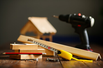 Wooden house on a wooden surface made of boards and tools, tape measure, screwdriver, pencil....
