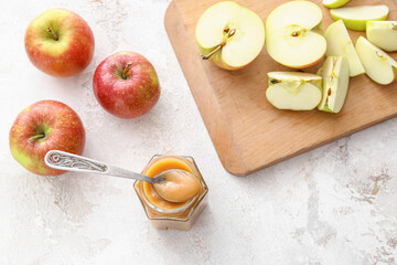 Jar of sweet apple jam and spoon on light background