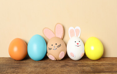 Two eggs as bunnies among others on wooden table against beige background. Easter celebration