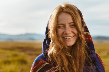 girl wrapped in plaid with red hair and freckles on her face gently and kindly smiles against the...