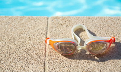 Fototapeta na wymiar Swimming goggles lie at the edge of the blue pool on a sunny day